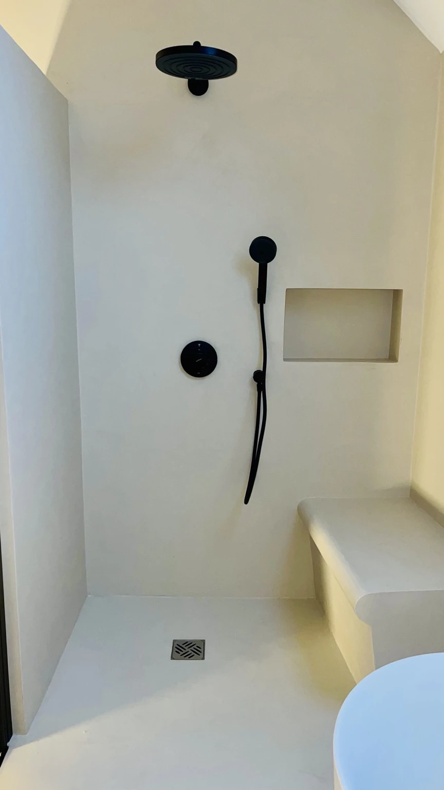 Helle Dusche mit runden schwarzen Armaturen, Wandnische und integrierter Sitzbank